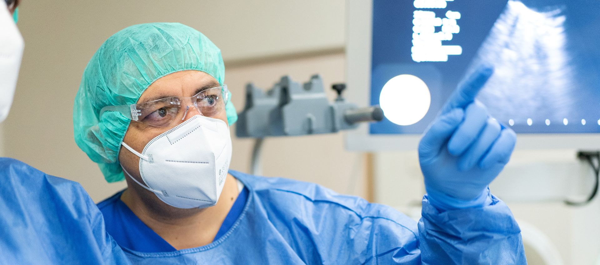 Dr. Othman in medizinischer Ausrüstung zeigt auf Monitor