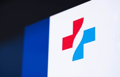 Das Logo des Klinikverbundes, ein rot-blaues Kreuz, ist groß auf einer Glasfläche sichtbar angebracht.