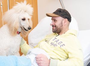 Feodora liegt auf ihrer Spezialdecke im Patientenbett, während der Patient ihren Kopf streichelt.