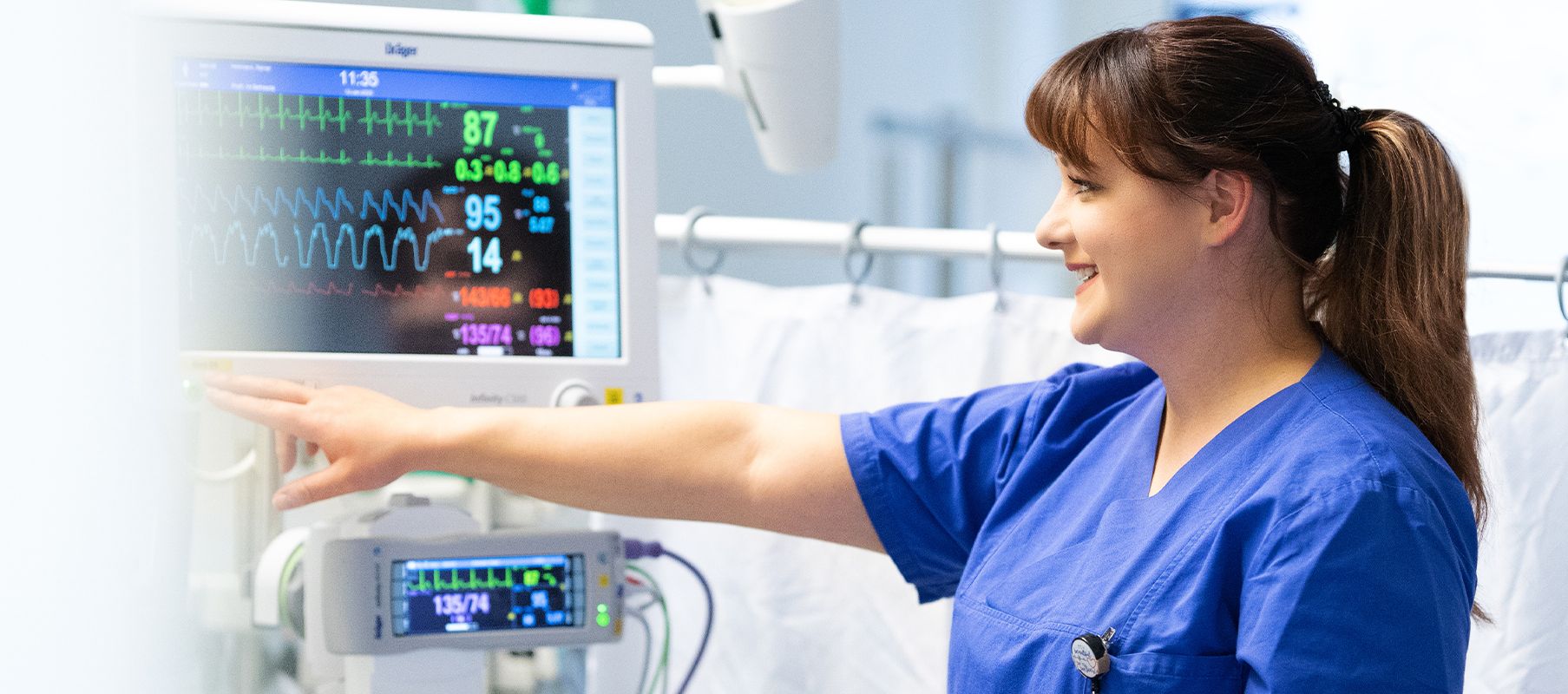Pflegerin auf der Intensivstation neben einem Patientenbett mit Monitor.