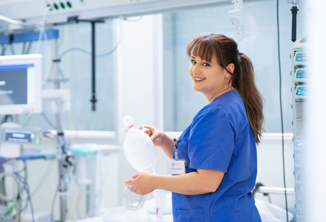Pflegerin auf der Intensivstation neben einem Patientenbett mit Beatmungsbeutel.